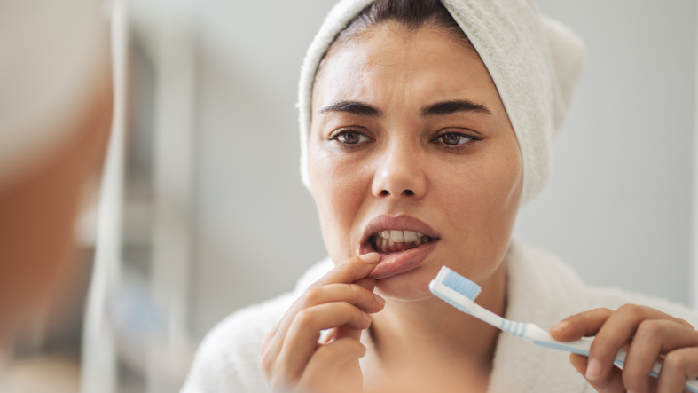Young woman looking at her bleeding gums while brushing teeth.