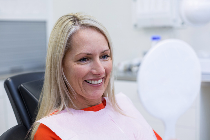 Happy patient checking her dental implant in mirror at periodontist office.